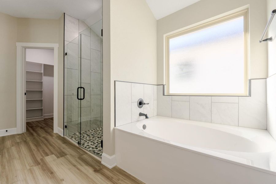 Full bath featuring a walk in closet, a stall shower, a bath, and light wood-type flooring