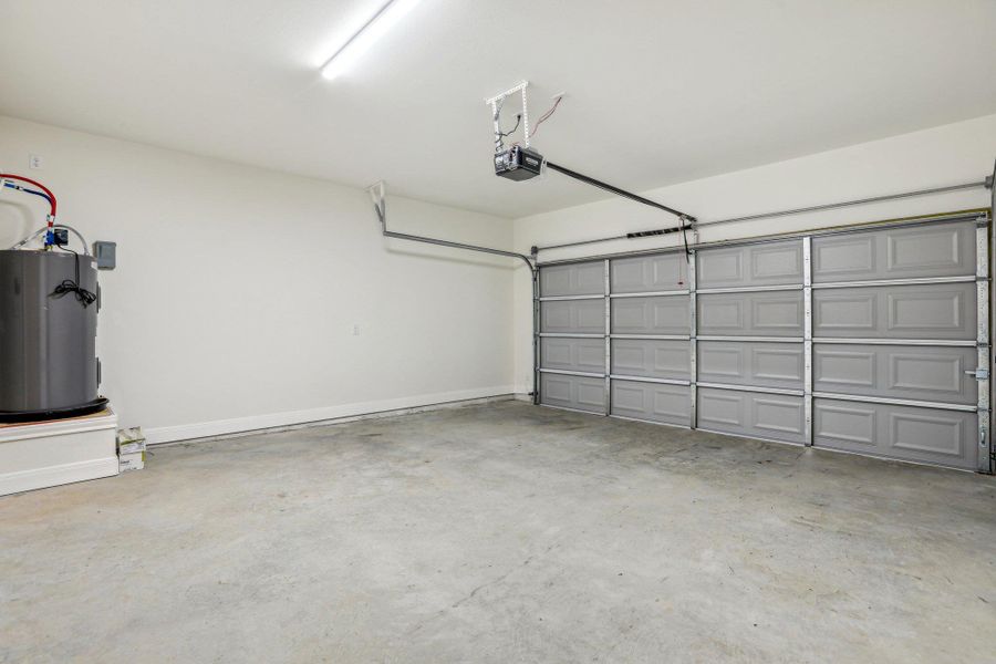 Garage featuring water heater, baseboards, and a garage door opener