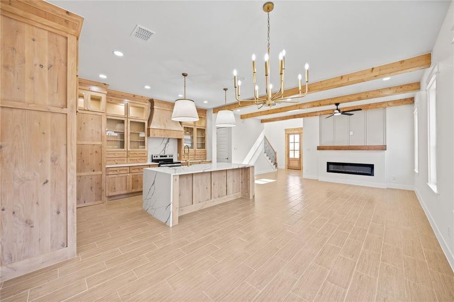 Kitchen with light wood finish cabinets, glass insert cabinets, a chandelier, a glass covered fireplace, and a large island Kitchen with light wood finish cabinets, glass insert cabinets, a chandelier, a glass covered fireplace, and a large island