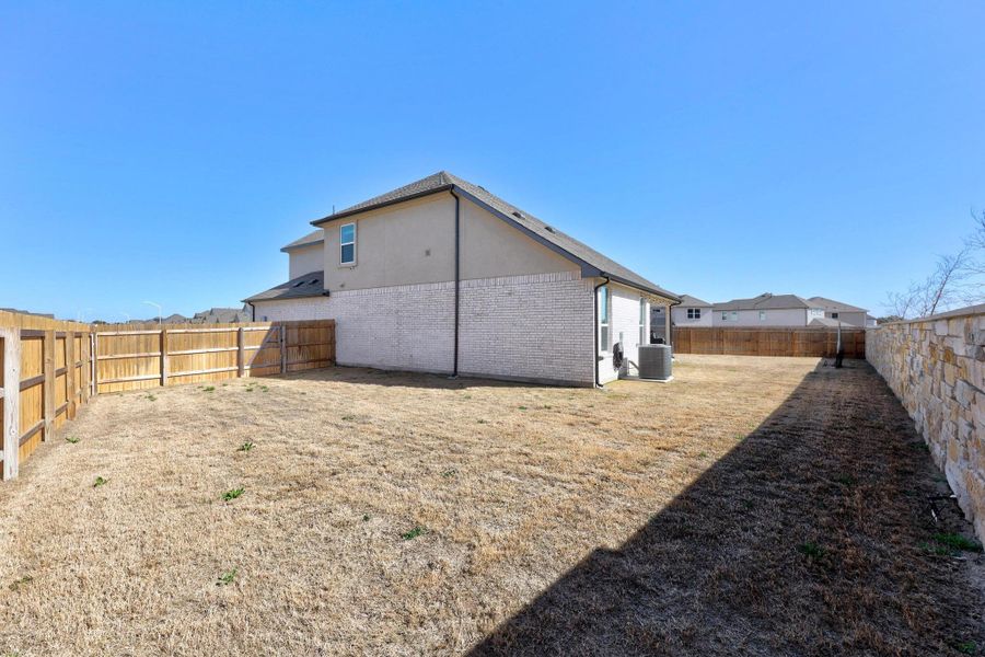 Back of house featuring a large cul de sac yard, brick fence, and a  completely fenced backyard.