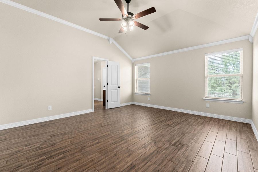 Empty room featuring crown molding, dark wood like tile floors, lofted ceiling, and a ceiling fan Empty room featuring crown molding, dark wood like tile floors, lofted ceiling, and a ceiling fan