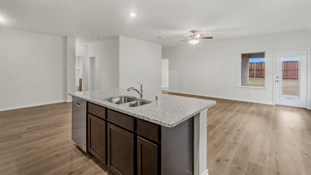 Kitchen featuring dark brown cabinets, light stone countertops, open floor plan, and light wood finished floors Kitchen featuring dark brown cabinets, light stone countertops, open floor plan, and light wood finished floors