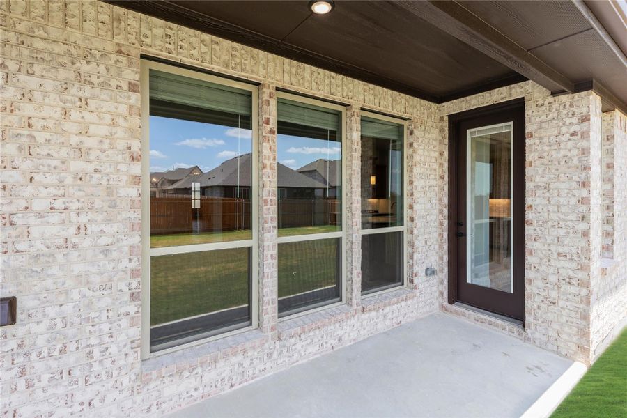 Covered back patio with concrete floor, large windows, and dark door on light brick exterior wall Covered back patio with concrete floor, large windows, and dark door on light brick exterior wall
