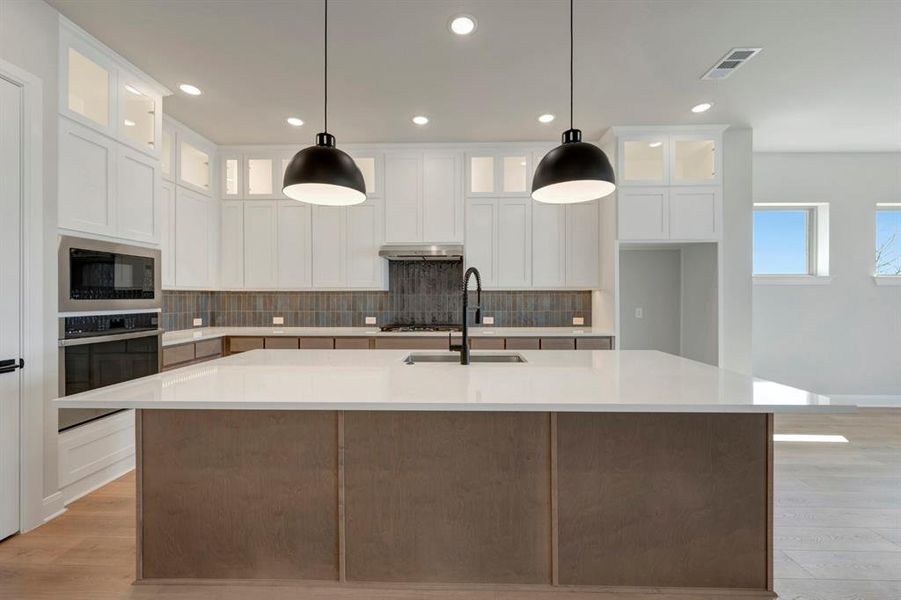 Kitchen with tasteful backsplash, glass insert cabinets, an island with sink, stainless steel appliances, and dual tone cabinets