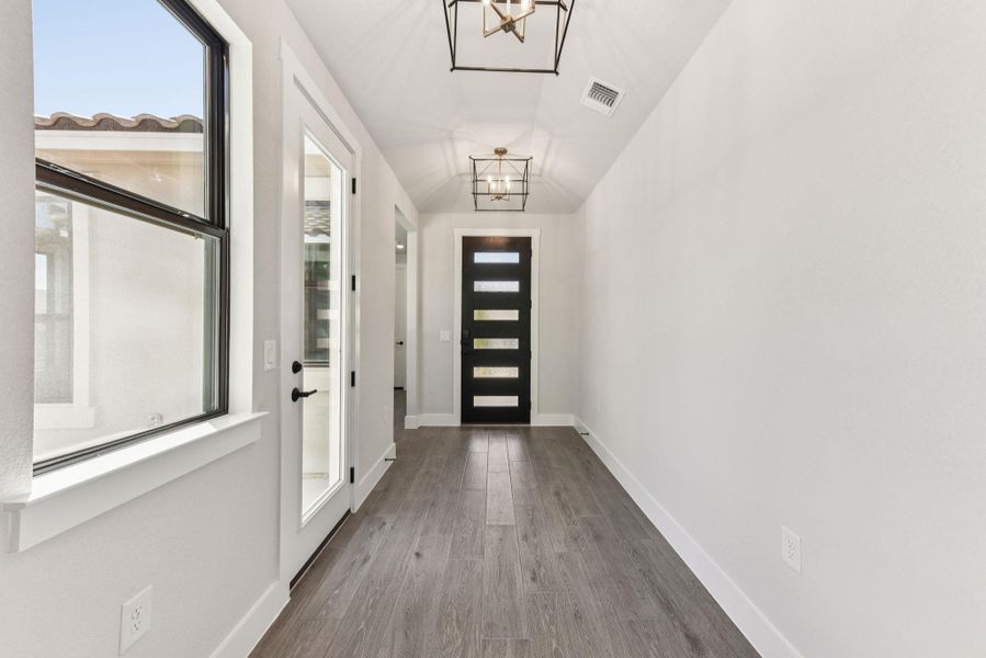 Doorway to outside with wood finished floors, a chandelier, and vaulted ceiling