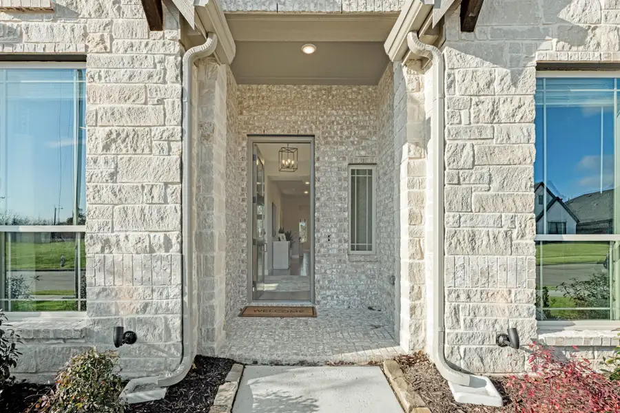 Home entrance with light stone exterior, glass front door, covered porch, and welcome mat leading to bright interior hallway. Home entrance with light stone exterior, glass front door, covered porch, and welcome mat leading to bright interior hallway.