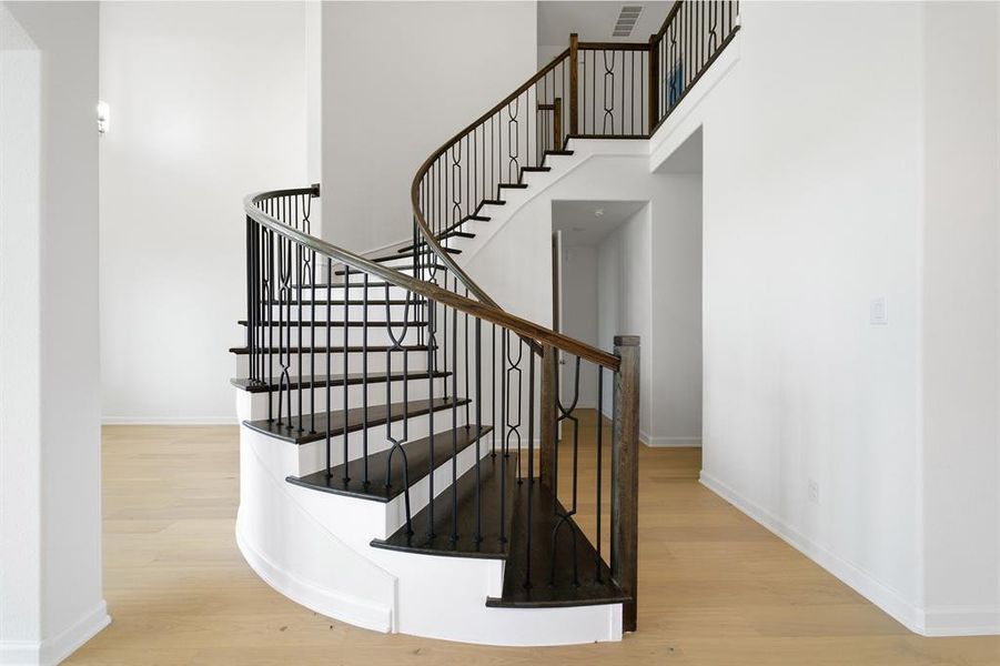 Grand spiral staircase featuring dark wood-finish treads, white risers, and wrought iron balusters with a decorative pattern