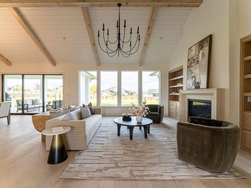 Living room with a glass covered fireplace, light wood-style flooring, a chandelier, high vaulted ceiling, and built in features