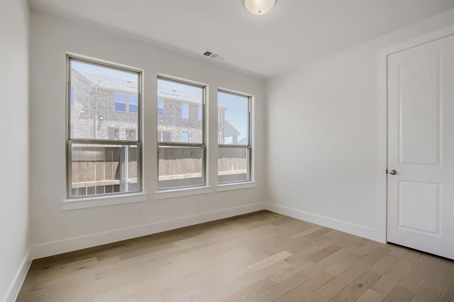 Room featuring three large windows, light wood-finish flooring, white baseboards, a white paneled door, and a flush-mount ceiling light fixture