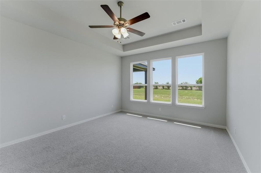 Spacious room featuring light gray carpeting, neutral wall finishes, and a tray ceiling with a ceiling fan Spacious room featuring light gray carpeting, neutral wall finishes, and a tray ceiling with a ceiling fan