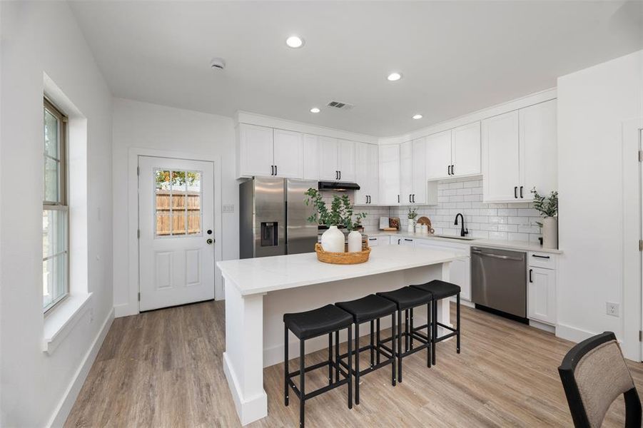 Kitchen with a breakfast bar area, white cabinets, backsplash, light wood-type flooring, and stainless steel appliances Kitchen with a breakfast bar area, white cabinets, backsplash, light wood-type flooring, and stainless steel appliances