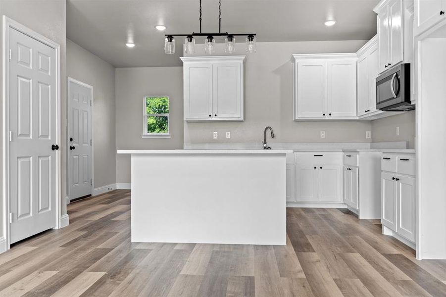 Kitchen featuring stainless steel microwave, light wood-style flooring, light countertops, and white cabinetry Kitchen featuring stainless steel microwave, light wood-style flooring, light countertops, and white cabinetry