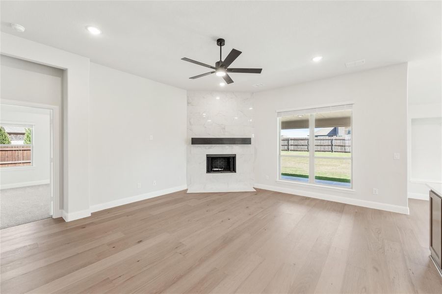 Open living room with light hardwood floors, marble fireplace, ceiling fan, and backyard window view
