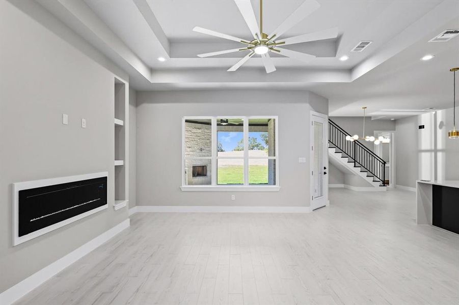 Unfurnished living room featuring a chandelier, light wood-type flooring, ceiling fan, recessed lighting, and stairway