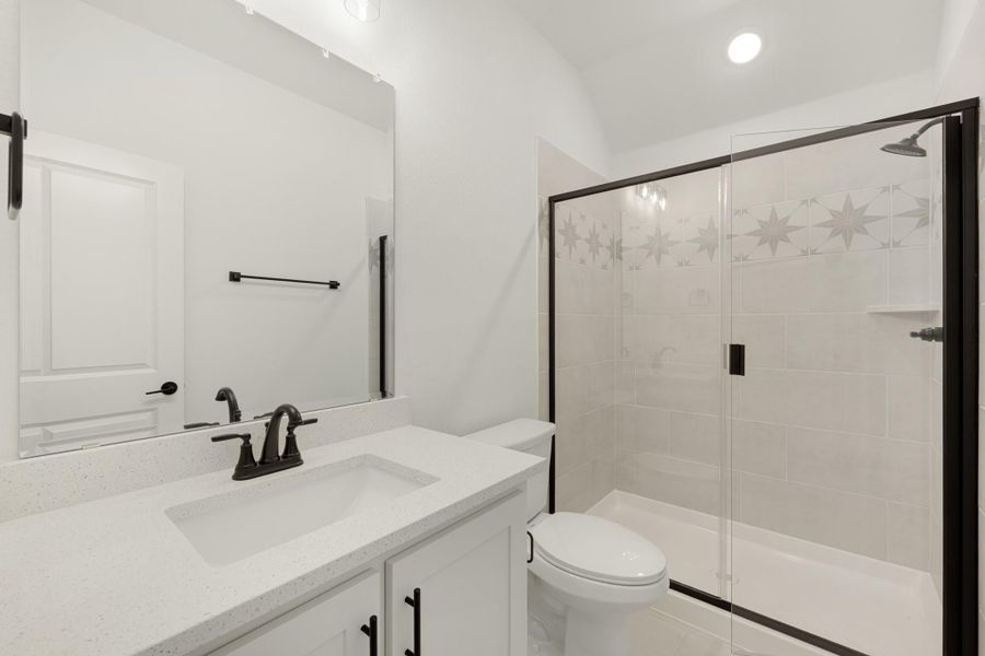 Bathroom with white quartz vanity, black fixtures, and glass-enclosed shower with star tile accent border.