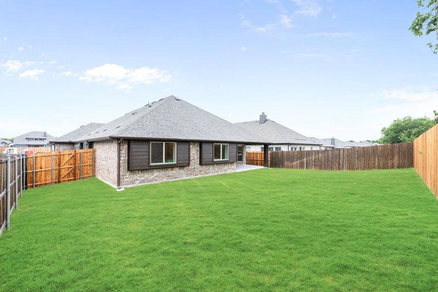 Backyard of single-story brick home with large green lawn and wood privacy fence