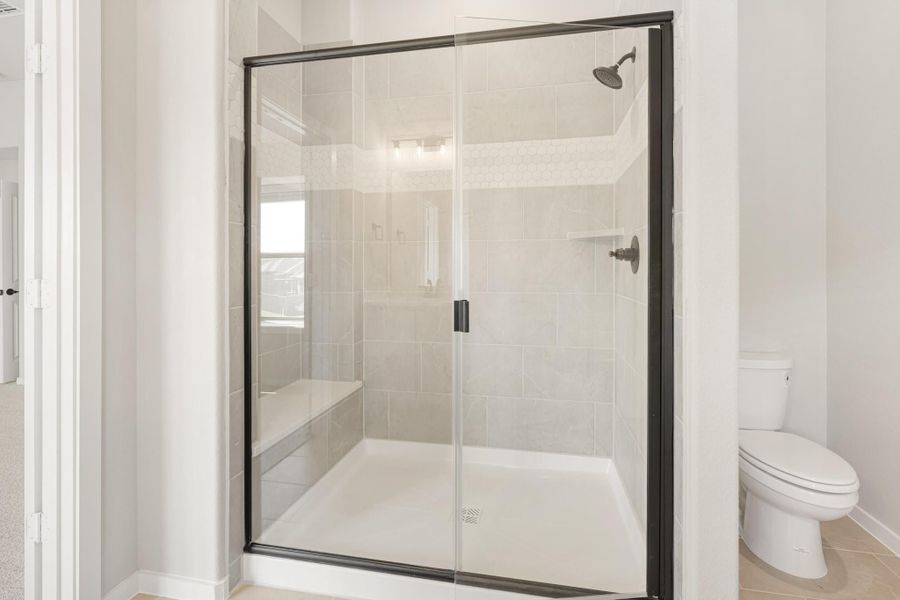 Walk-in shower with black-framed glass doors, light tile walls, built-in bench, and rain showerhead next to a white toilet