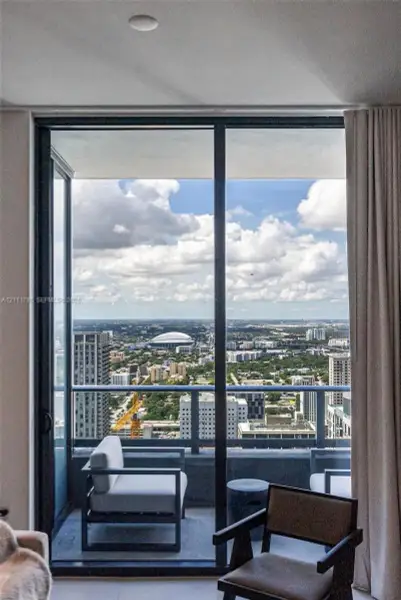 Floor-to-ceiling sliding glass door opening to a private balcony with a metal railing and expansive urban cityscape backdrop