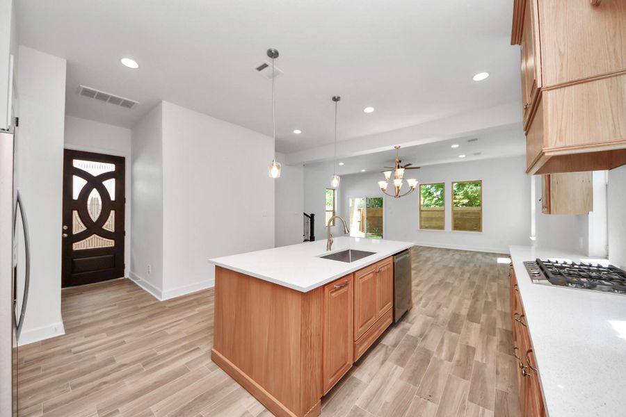 Modern, open-concept kitchen and living area with ceramic flooring, a quartz central island with a sink, and ample natural light from large windows. The kitchen features sleek countertops, a gas cooktop, and contemporary lighting fixtures, creating a bright and inviting space.