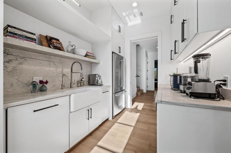 Kitchen featuring white cabinetry, open shelves, light stone countertops, high end refrigerator, and light wood-style flooring Kitchen featuring white cabinetry, open shelves, light stone countertops, high end refrigerator, and light wood-style flooring