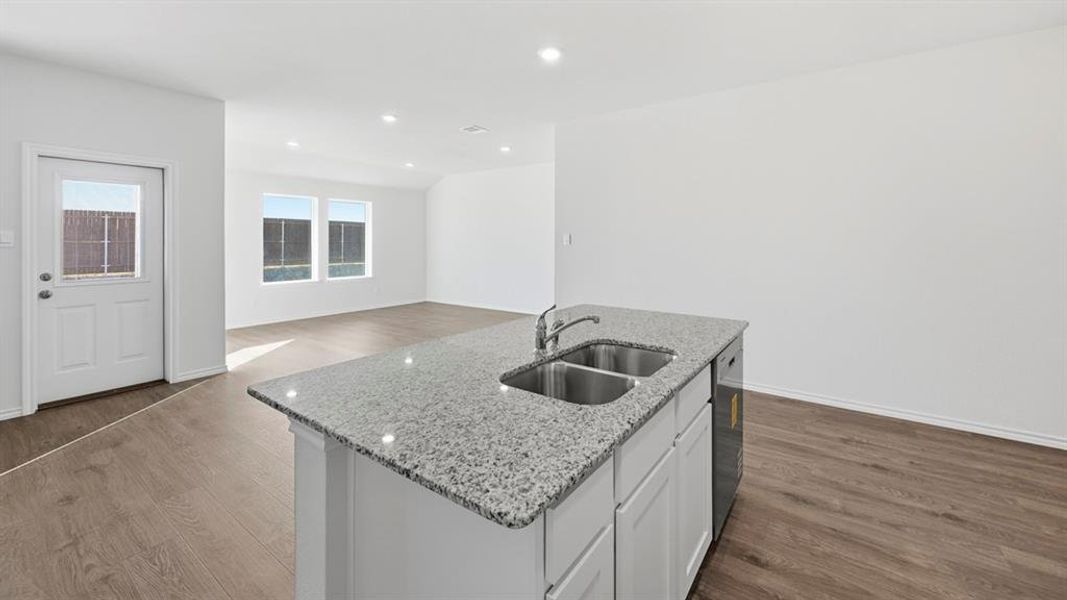 Kitchen featuring light stone counters, a center island with sink, dark wood-type flooring, white cabinetry, and open floor plan