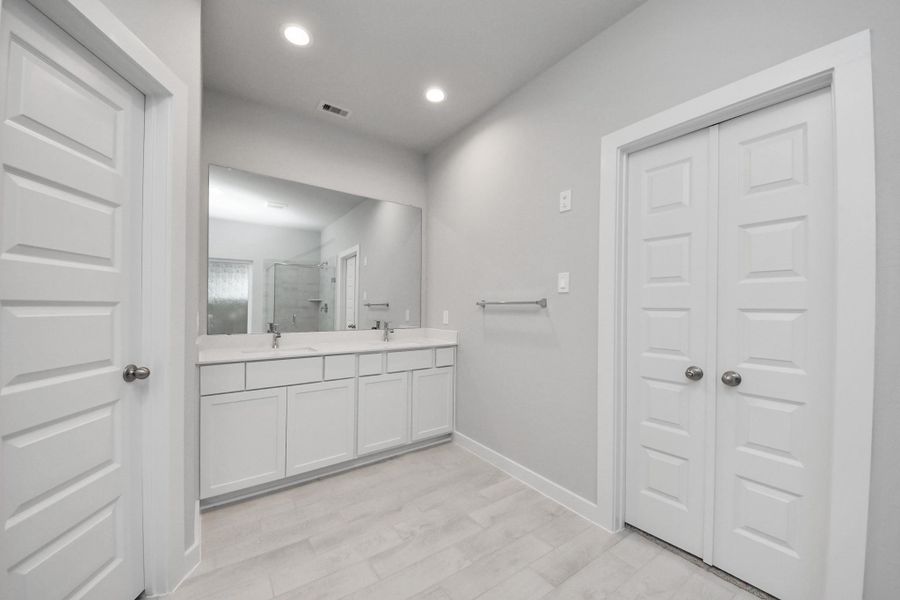Escape to a spa-like oasis in this primary bathroom. Enjoy a walk-in shower with tile surround, a separate garden tub with custom detailing, and an elegant vanity featuring light countertops, modern hardware, and beautiful vanity lights. Experience luxury and relaxation in every detail. Sample photo of completed home with similar floor plan. Actual colors and selections may vary.