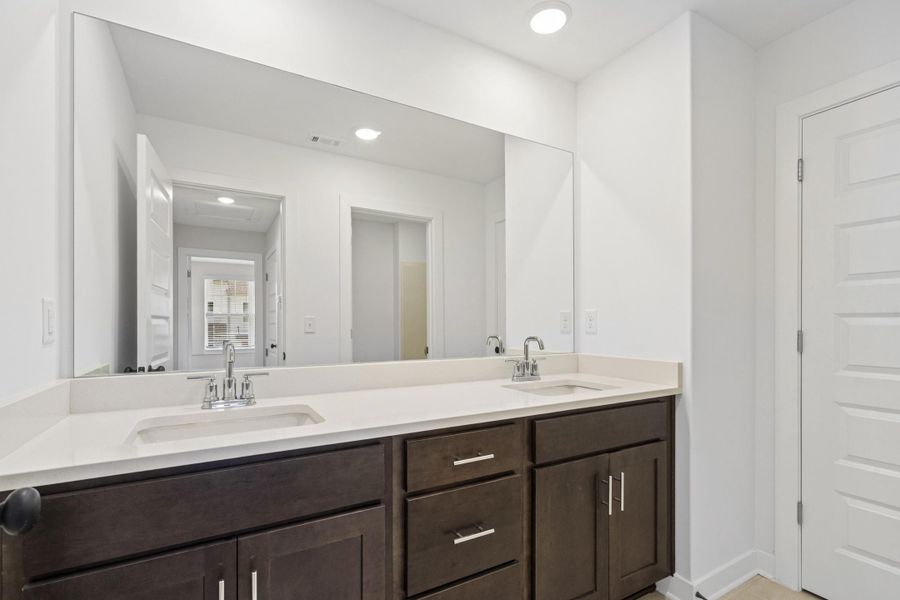 Double vanity featuring a wide mirror, two integrated sinks, stone-finish countertop, and dark wood cabinetry with chrome hardware
