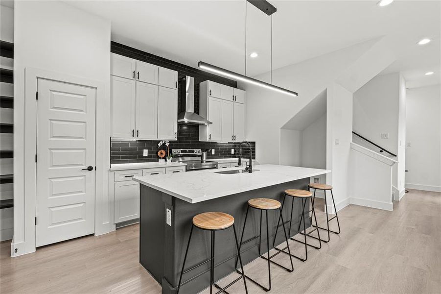 Kitchen featuring stainless steel electric range, sink, an island with sink, white cabinets, and wall chimney exhaust hood