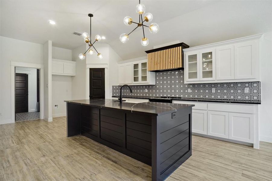 Kitchen with light hardwood / wood-style floors, white cabinets, tasteful backsplash, and an island with sink