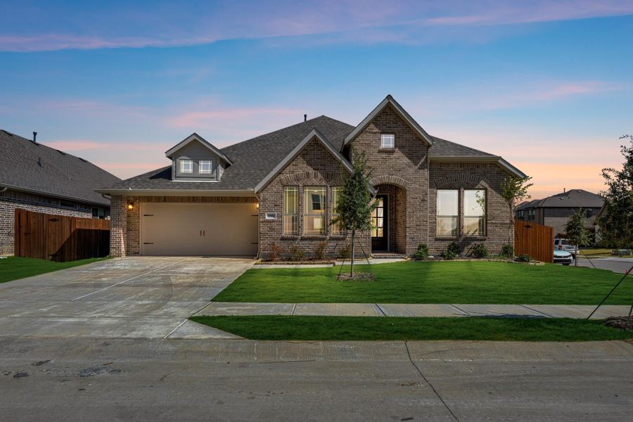 Single-story brick home with two-car garage, arched entry, and green front lawn at dusk.