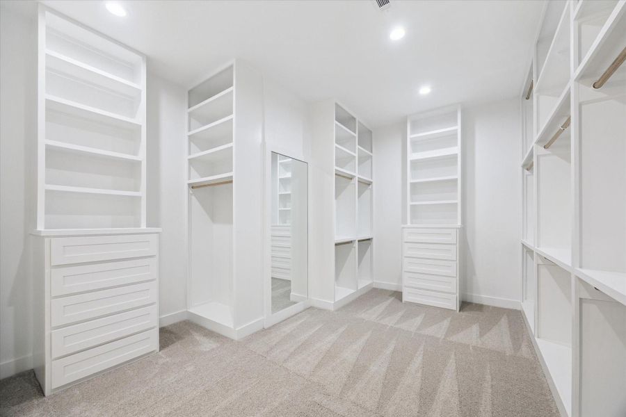 This oversized walk-in closet offers custom built-ins, abundant hanging space, soft carpet underfoot, and a full-length mirror delivering both luxury and organization in one beautifully designed space. This oversized walk-in closet offers custom built-ins, abundant hanging space, soft carpet underfoot, and a full-length mirror delivering both luxury and organization in one beautifully designed space.