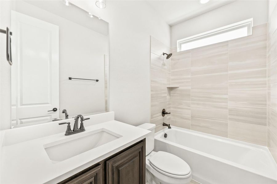 Bathroom with white quartz vanity, dark wood cabinets, and tiled tub-shower combo with small window Bathroom with white quartz vanity, dark wood cabinets, and tiled tub-shower combo with small window