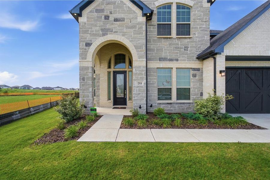 Stone and brick facade featuring an arched entry, dark panel garage door, and a concrete pathway with planted landscaping