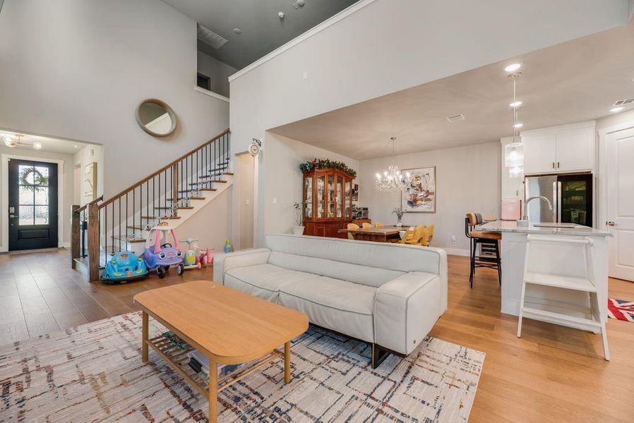 Living area with light wood-type flooring, hanging lights, and a high ceiling