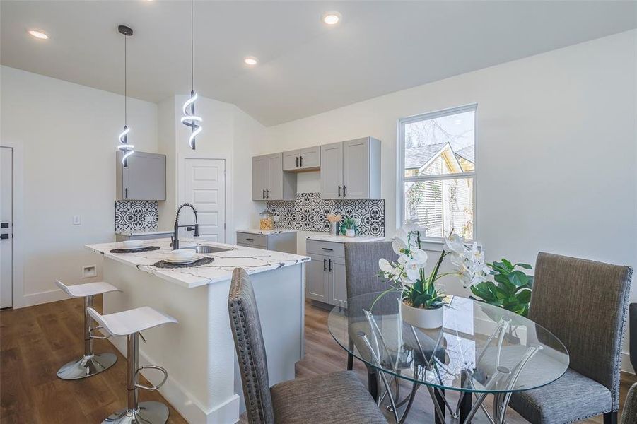 Kitchen featuring gray cabinetry, hanging light fixtures, light stone counters, an island with sink, and dark hardwood / wood-style flooring