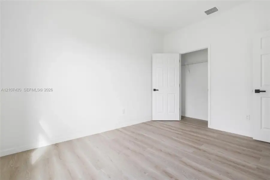 Neutral-toned wood-finish flooring, white walls, and interior doors featuring matte black hardware, including a closet with wire shelving Neutral-toned wood-finish flooring, white walls, and interior doors featuring matte black hardware, including a closet with wire shelving