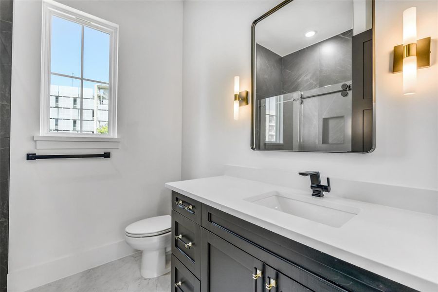 The ensuite bathroom continues the home’s luxury aesthetic with quartz countertops, black shaker cabinetry, and brushed brass hardware and lighting. The frameless glass shower enclosure is fully tiled in marble-pattern porcelain, featuring a brass sliding door system, recessed shampoo niche, and designer fixtures. Every element blends craftsmanship with timeless design for a spa-quality experience in a private setting. The ensuite bathroom continues the home’s luxury aesthetic with quartz countertops, black shaker cabinetry, and brushed brass hardware and lighting. The frameless glass shower enclosure is fully tiled in marble-pattern porcelain, featuring a brass sliding door system, recessed shampoo niche, and designer fixtures. Every element blends craftsmanship with timeless design for a spa-quality experience in a private setting.