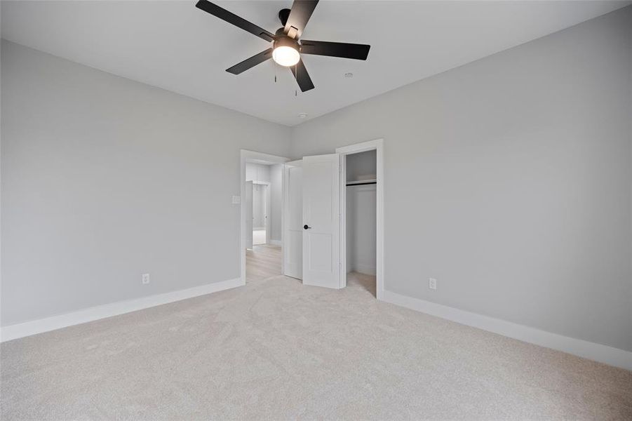 Unfurnished bedroom with a closet, light colored carpet, baseboards, and ceiling fan