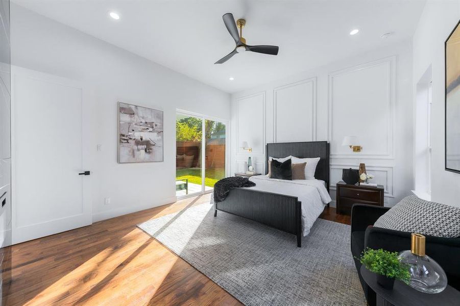 Large primary bedroom with red oak wood floors, access to outside, a ceiling fan, wainscoting, recessed lighting and wall mounted sconces. Large primary bedroom with red oak wood floors, access to outside, a ceiling fan, wainscoting, recessed lighting and wall mounted sconces.