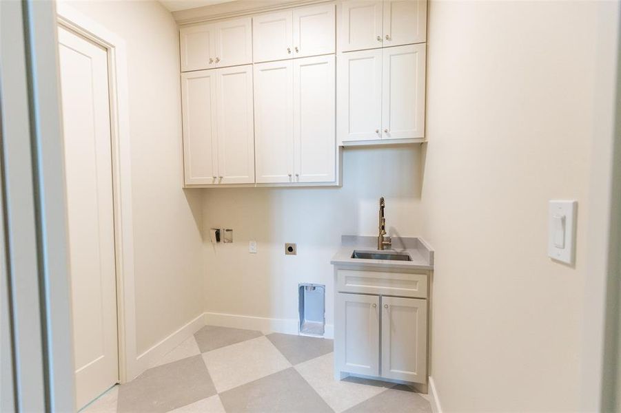 Laundry room featuring white shaker cabinetry, an undermount sink with a gooseneck faucet, light-toned countertop, and patterned floor tiling