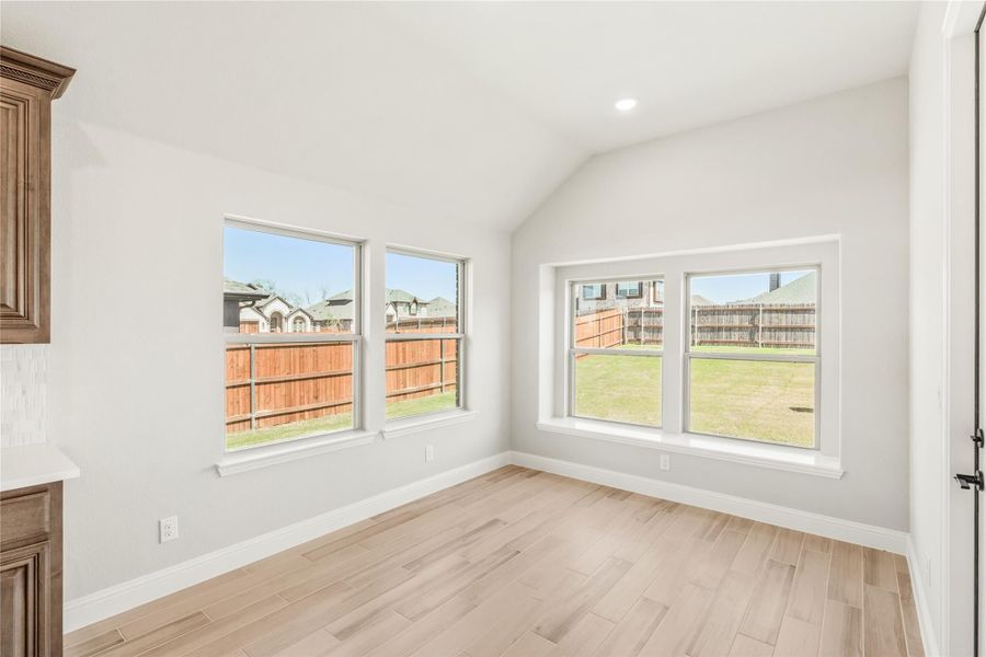 Empty room with vaulted ceiling, light wood floors, and three windows overlooking fenced backyard Empty room with vaulted ceiling, light wood floors, and three windows overlooking fenced backyard