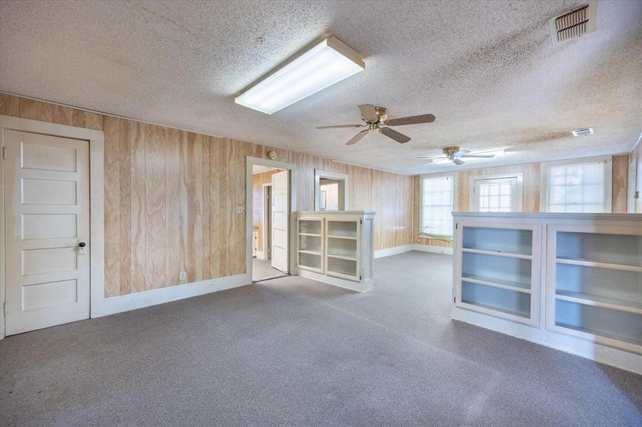 Unfurnished room with ceiling fan, wood walls, a textured ceiling, and light carpet