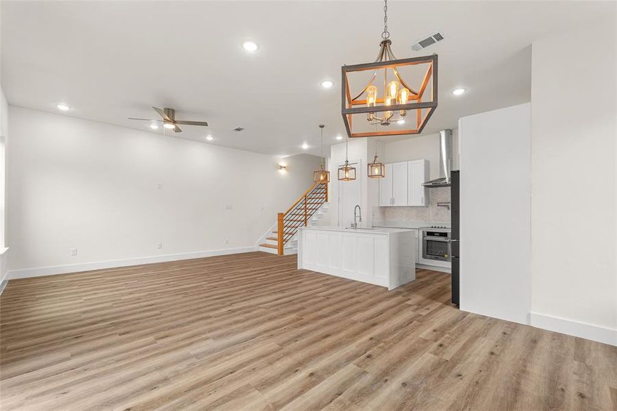 Unfurnished living room with stairs, recessed lighting, a ceiling fan, light wood-style floors, and a chandelier Unfurnished living room with stairs, recessed lighting, a ceiling fan, light wood-style floors, and a chandelier