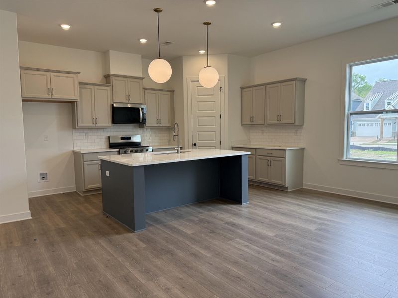 Open-concept kitchen featuring an oversized island with a white countertop, stainless steel appliances, light gray cabinetry, subway tile backsplash, and wood-finish flooring