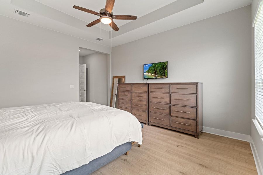Bedroom with a raised ceiling, wood finished floors, and a ceiling fan Bedroom with a raised ceiling, wood finished floors, and a ceiling fan