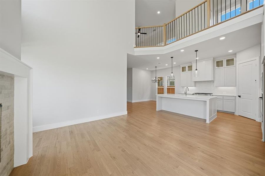 Unfurnished living room featuring a high ceiling, light wood finished floors, recessed lighting, a fireplace, and a chandelier