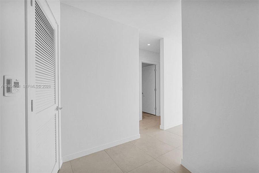 Louvered door, neutral tile flooring, recessed lighting, and crisp white walls