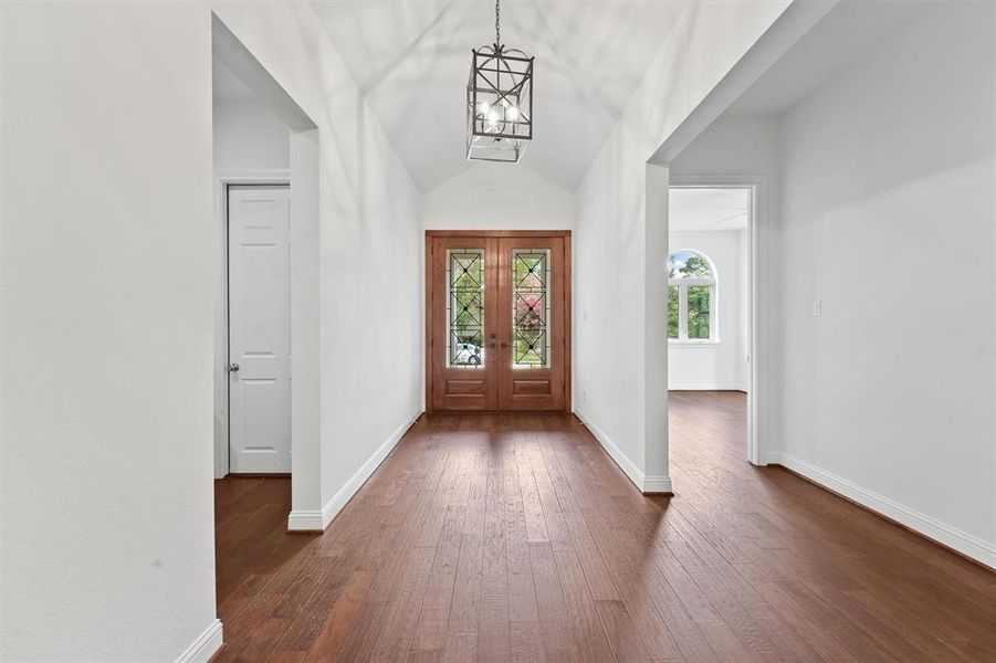 Bright, airy entryway with high vaulted ceilings, hardwood floors, and an elegant front door with stained glass panels. There are multiple entry points leading to adjacent rooms, creating an open and versatile floor plan.