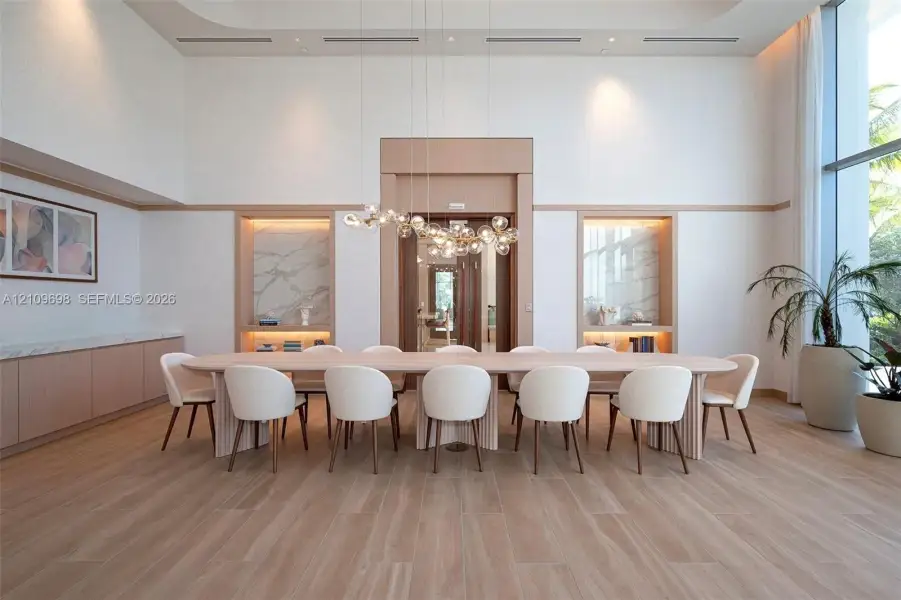 High-ceilinged room featuring wood-finish flooring, dual built-in shelving niches with stone-slab backsplashes, custom millwork, and an intricate multi-globe chandelier