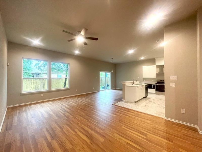 Unfurnished living room featuring a sink, light wood-style flooring, a ceiling fan, and baseboards